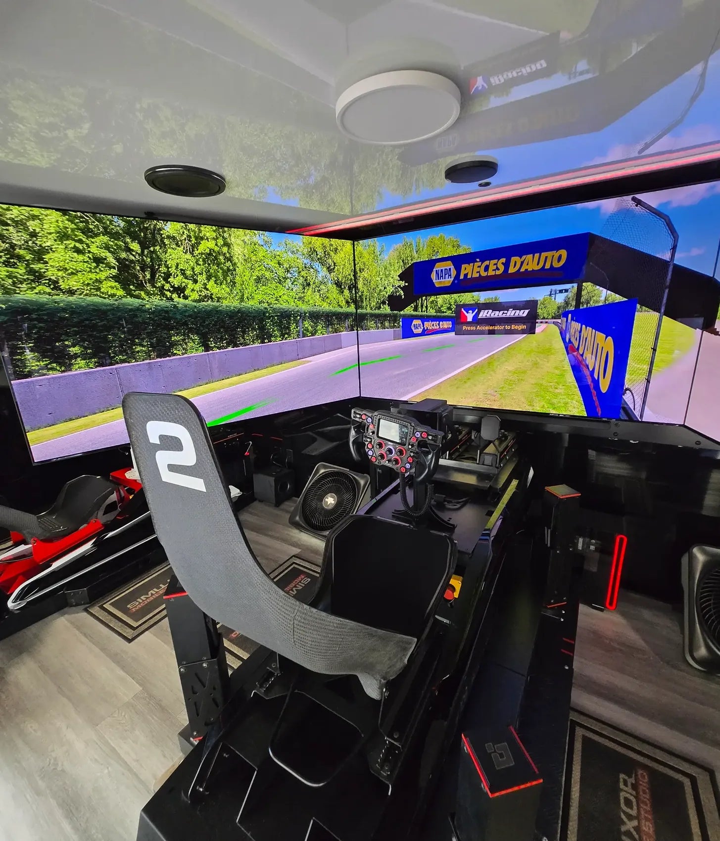 Two adjacent simulator seats and triple-screen displays inside the Mobile Race Studio
